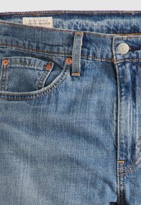 Jean en denim bleu avec poches avant visibles, passants de ceinture, bouton en métal et étiquette de vêtement premium Levi's à l'intérieur de la ceinture.