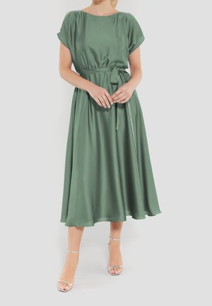 Robe verte en satin, de coupe A, avec des manches courtes, une taille cintrée et un ourlet fluide. Présente une texture lisse et un décolleté rond.