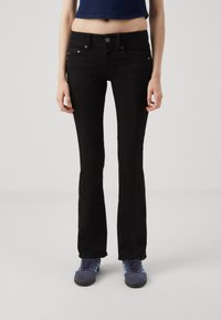 Pantalones vaqueros de campana negros con una cintura ajustada y bolsillos frontales, hechos de tela de mezclilla. Combinados con zapatillas atléticas azules con rayas.