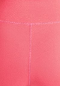 Close-up van roze sportlegging met een gladde textuur, platte naden en een aansluitend ontwerp voor comfort en flexibiliteit.