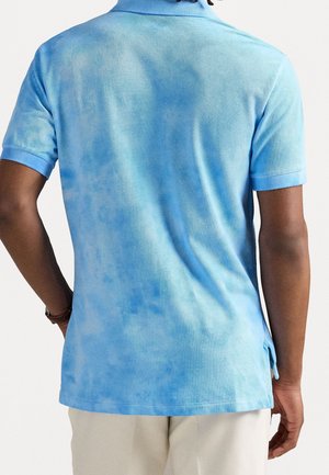 Polo paita lyhyillä hihoilla, jossa on liukuväri vaaleansininen, valmistettu kuviosta. Sisältää kauluksen ja sivuhalkiot mukavuutta varten.