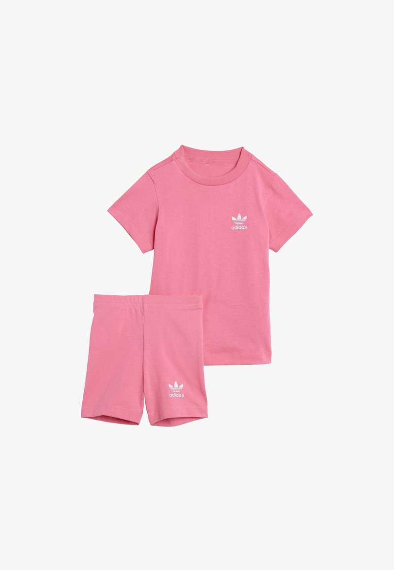 Ružová bavlnená súprava trička a šortiek s okrúhlym výstrihom, krátkymi rukávmi a bielym logom na hrudi a na nohaviciach. Jemná textura.