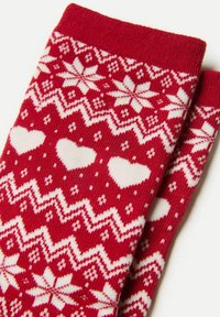 Røde strikkede sokker med et hvidt mønster af hjerter, snefnug og zigzag-linjer. Den øverste kant er ribbet for ekstra tekstur.