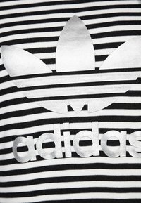 Černobílý pruhovaný svetr s velkým stříbrným logem Adidas, které doplňují tři listovité akcenty a vyražené písmo.