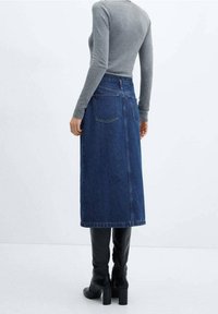 Rok denim berwarna gelap, panjang hingga lutut dengan kantong belakang dan potongan lurus. Dipasangkan dengan atasan lengan panjang abu-abu yang pas dan sepatu bot hitam setinggi lutut.