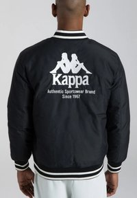 Giacca bomber nera con logo ricamato bianco sul retro, colletto e polsini a coste a righe in contrasto, con una texture liscia.