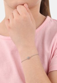 Bracciale d'argento con un design a fiocco di neve, dotato di una pietra blu centrale e una delicata catena, indossato su un polso. Lo sfondo è semplice.