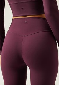 Burgundy athletic set featuring a long-sleeve top and high-waisted leggings. Smooth fabric with embedded logo accents. Close-fitting design.
