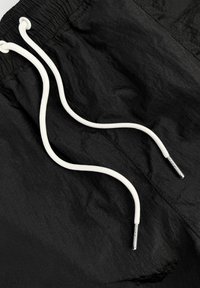 Zwarte shorts gemaakt van lichtgewicht materiaal, voorzien van witte koorden met metalen uiteinden. De stof heeft een licht gekreukt textuur.