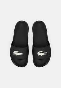 Sandales noires à glissière en matériau synthétique lisse, avec un logo de crocodile blanc sur la bride et une semelle intérieure texturée pour plus de confort.
