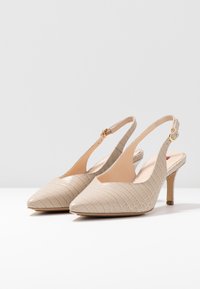 Talons slingback beiges avec un bout pointu, motif croco texturé et un talon fin. Équipés d'une bride ajustable à la cheville et d'une semelle intérieure lisse.