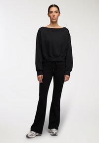 Czarny, oversize sweatshirt z szerokim dekoltem, ryżowym wykończeniem i długimi rękawami, zestawiony z dopasowanymi czarnymi spodniami i srebrnymi butami sportowymi.