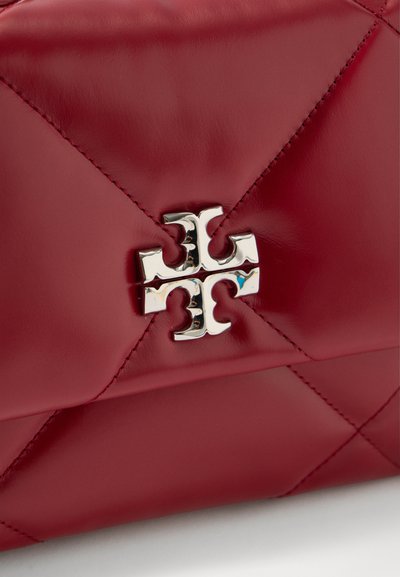 Κόκκινη επενδεδυμένη δερμάτινη επιφάνεια με διαγώνια ραφή και λαμπερό ασημένιο διακριτικό σε σχήμα σταυρού στο κέντρο.