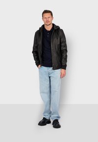 Sort læderjakke med hætte, marineblå polo, lyseblå jeans og sorte sko. Jakken har lynlås og sidelommer.