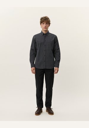 Black and white striped button-up shirt with long sleeves, featuring a chest pocket, paired with black trousers and brown shoes.