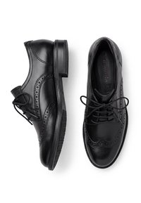 Ζευγάρι μαύρα δερμάτινα παπούτσια brogue με κορδόνια, που δείχνει πλάγια όψη του αριστερού παπουτσιού και πάνω όψη του δεξιού παπουτσιού σε λευκό φόντο.