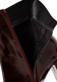 Bottine bordeaux brillante avec un extérieur brillant, doublure texturée noire et détail de zip rouge. L'intérieur est composé d'un matériau doux et semblable à de la fourrure foncée.