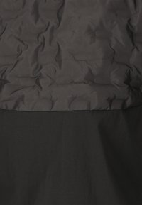Schwarze Pufferjacke mit einem gesteppten Design im oberen Bereich und einem glatten Stoff im unteren Bereich, beide in verschiedenen Schattierungen von Schwarz.