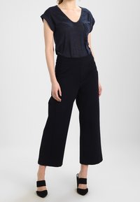 Dark blue V-neck T-shirt with short sleeves, paired with high-waisted black wide-leg pants. Worn with black heeled shoes. Smooth texture.