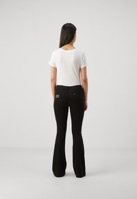 Valkoinen lyhythihainen t-paita yhdistettynä mustiin liehuviin farkkuihin, joissa on takataskut ja vyötärönauhassa brändilogo. Yksinkertainen malli ja hillityt värit.