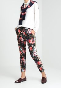 Blommönstrade byxor med svart botten, prydda med färgglada rosor. Sidosträck i vitt och guld, i kombination med en vit topp och en marinblå scarf.
