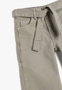 Beige bomullbyxor med rak design, bältesöglor och ett tygbälte. Har två framfickor och en strukturerad yta.