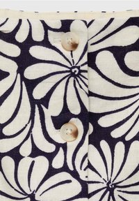 Gros plan d’un tissu avec un motif floral abstrait en noir et blanc et deux boutons beiges translucides cousus sur une patte verticale.