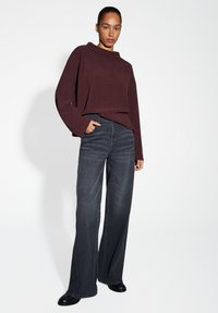 Bordeaux oversized trui met een hoge halslijn, gecombineerd met donkerblauwe wijde jeans en zwarte enkellaarsjes. Glad textuur van de stof.