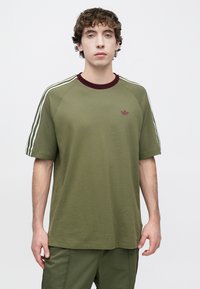 Πράσινο ελιάς ανδρικό μπλουζάκι με κοντά μανίκια, ριμπ μπορντό λαιμόκοψη και άσπρες ρίγες στους ώμους. Μικρό μπορντό λογότυπο στο στήθος.