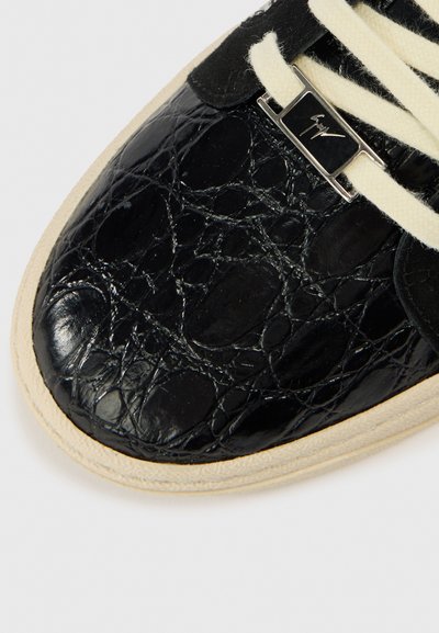 Μαύρο αθλητικό παπούτσι με δερμάτινη υφή που μοιάζει με δέρμα κροκοδείλου, κρεμ κορδόνια, μεταλλικό διακοσμητικό και μπεζ λαστιχένια σόλα.