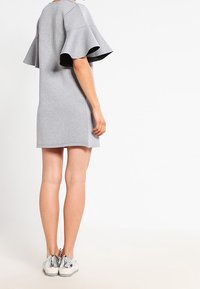 Harmaa lyhythihainen mekko, jossa on levenevät hihat, valmistettu pehmeästä kankaasta. Yhdistetty hopeisiin lenkkareihin, paljastaen jalat polveen asti.