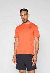 Camiseta atlética de manga corta de un vibrante color naranja, con un patrón de rayas diagonales texturizadas, que presenta un logo negro de Under Armour en el pecho.