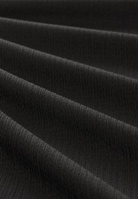 Tissu noir avec une fine texture côtelée verticale formant des plis doux en lignes parallèles et régulières.
