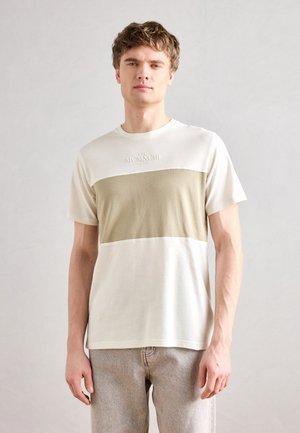 Tricou scurt cu mânecă, de culoare crem și verde măslin, cu blocuri de culoare orizontale și logo în relief pe partea superioară a pieptului. Material moale, casual.