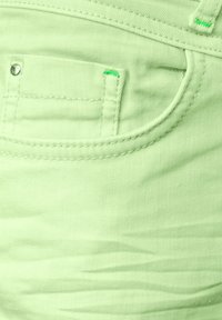 Jeans de algodón de color verde menta con acentos de costura, un bolsillo frontal y una textura suave. El hardware visible incluye un botón metálico.