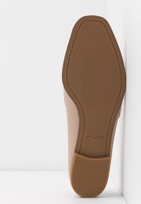 Semelle de chaussure beige avec un motif de grip texturé, présentant une forme arrondie et des détails de couture subtils. "ALDO" est embossé sur le talon.