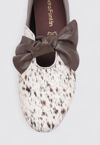 Chaussure à pois blancs et marron avec un bout rond, texture douce, et un grand nœud en cuir marron accentuant l'ouverture avant. Logo doré à l'intérieur.