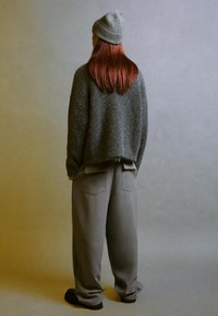 Berretto grigio a maglia e maglione grigio testurizzato, di forma oversize. Pantaloni grigi larghi con tasche posteriori, abbinati a calzature nere. Vista posteriore.