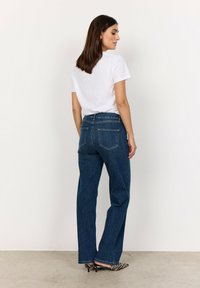 Korkeavyötäröiset tummansiniset farkut, jotka on valmistettu denimestä, suoranlahkeiset ja joissa on kaksi takataskua, yhdistettynä yksinkertaiseen valkoiseen lyhythihaiseen puseroon.