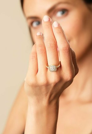 Goldnering mit quadratischem, mit Diamanten besetztem Mittelpunkt, ausgestattet mit einem glatten Band und strukturierten Details. Handpräsentation mit natürlichen Nägeln.