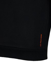 Fekete anyag bordás szegéllyel és kis függőleges narancssárga felirattal: "U.S. POLO ASSN." a alsó széle közelében.