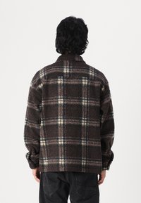 Veste en polaire à carreaux marron avec une texture douce, présentant un motif tartan en crème et vert foncé, et un design à col.