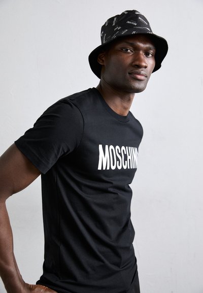 Svart T-skjorte med hvit "Moschino" logo, kombinert med en svart bøttehatt med hvite tekstmønstre. Jevn tekstur og tettsittende design.