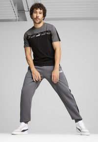 Svart och grå atletisk t-shirt med logotyp, kombinerad med gråa mjukisbyxor med sidostrippar och vita sneakers med svarta detaljer.