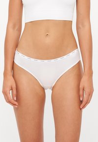 White women's briefs featuring a soft fabric, low-rise cut, and elastic waistband with "GUESS" logo printed in black.