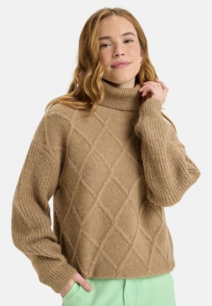 Pull en maille épaisse couleur beige avec un col roulé côtelé, un motif en losanges et des manches larges, fabriqué à partir d'un matériau doux et texturé.