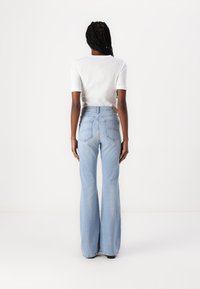 Jeans a vita alta di colore azzurro chiaro, svasati, con due tasche posteriori e dettagli di cucitura, abbinati a un top bianco a righe a manica corta.