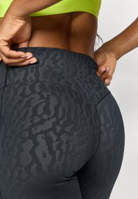 Højtaljede sorte leggings med en tekstureret, let skinnende overflade, der har et subtilt dyreprintmønster og flade sømme.