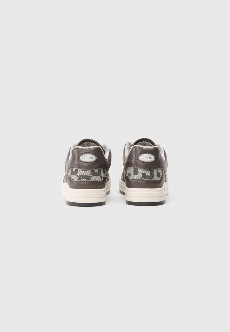 Sneaker marroni con un motivo testurizzato, pannelli in rete e accenti color crema. Presenta un'etichetta con il logo e una suola in gomma nera.