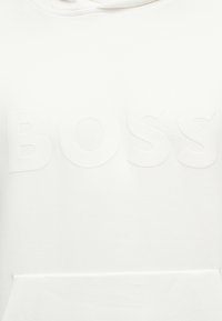 Λευκό ύφασμα με γυαλιστερό ανάγλυφο κείμενο "BOSS" στο κέντρο.